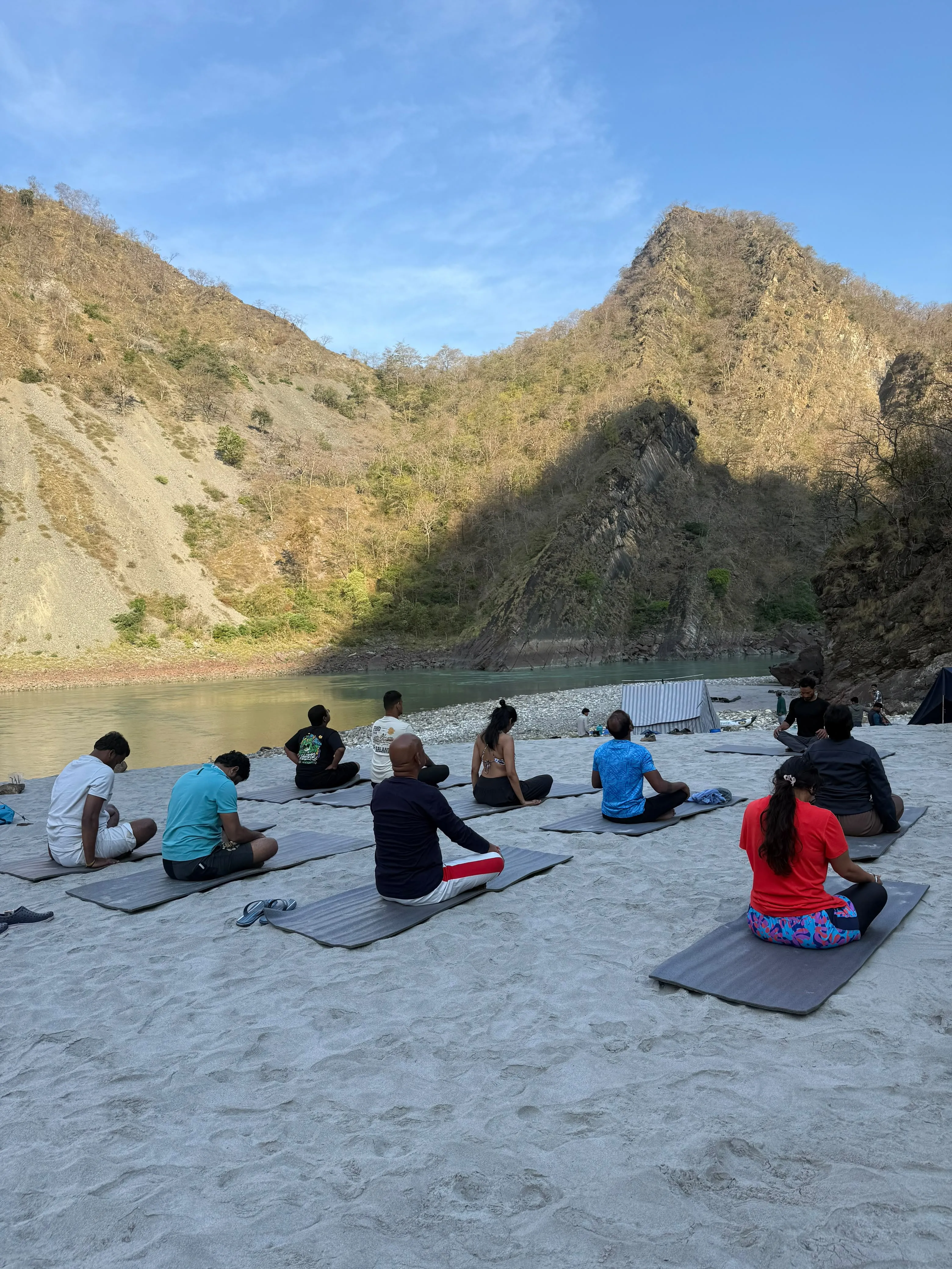 Guests practising yoga on the sands beside the Ganga in Rishikesh